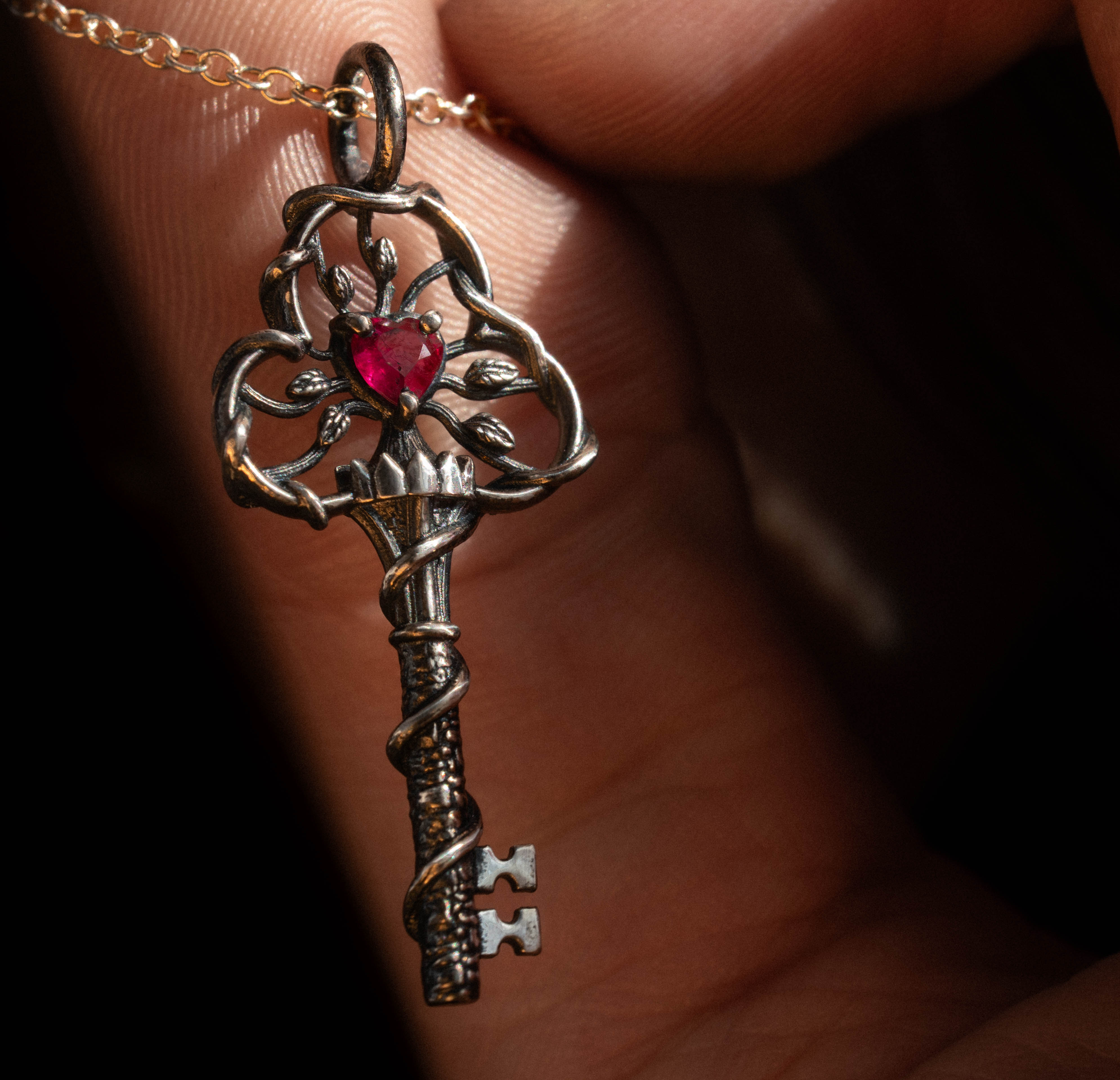 Macro detail of a Michaela Farkasovska Designs silver key pendant with a heart-cut ruby and vine filigree, held in the hand