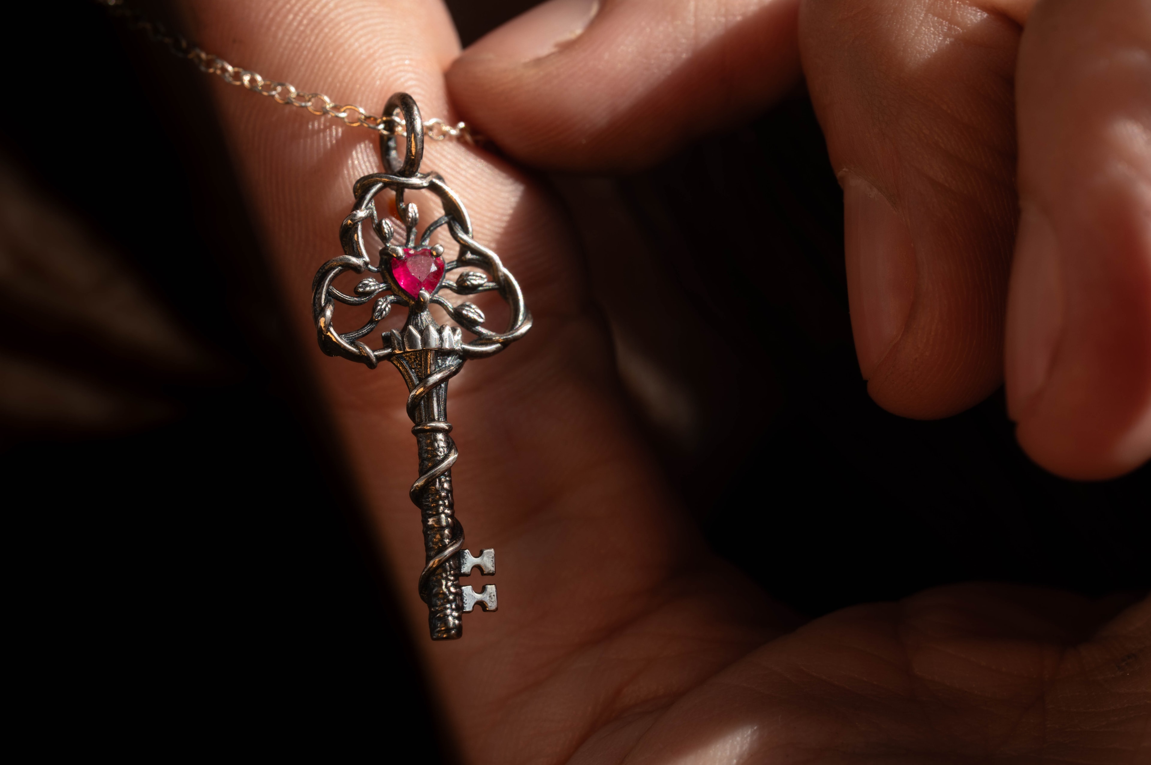 A handmade sterling silver key pendant set with a ruby by Michaela Farkasovska Designs, worn on a fine chain in warm afternoon light