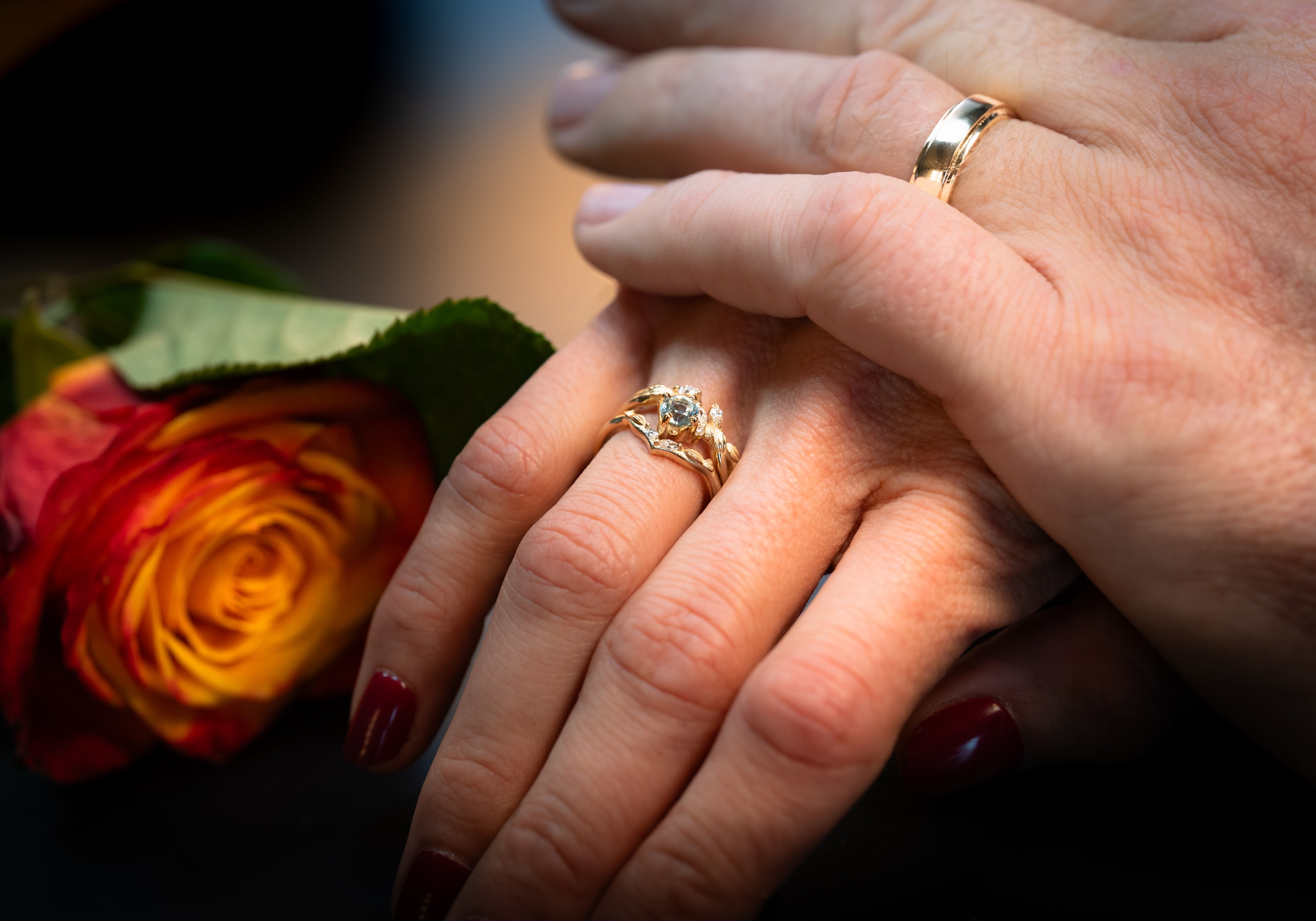 Wedding and engagement rings on a couple's hands beside a rose