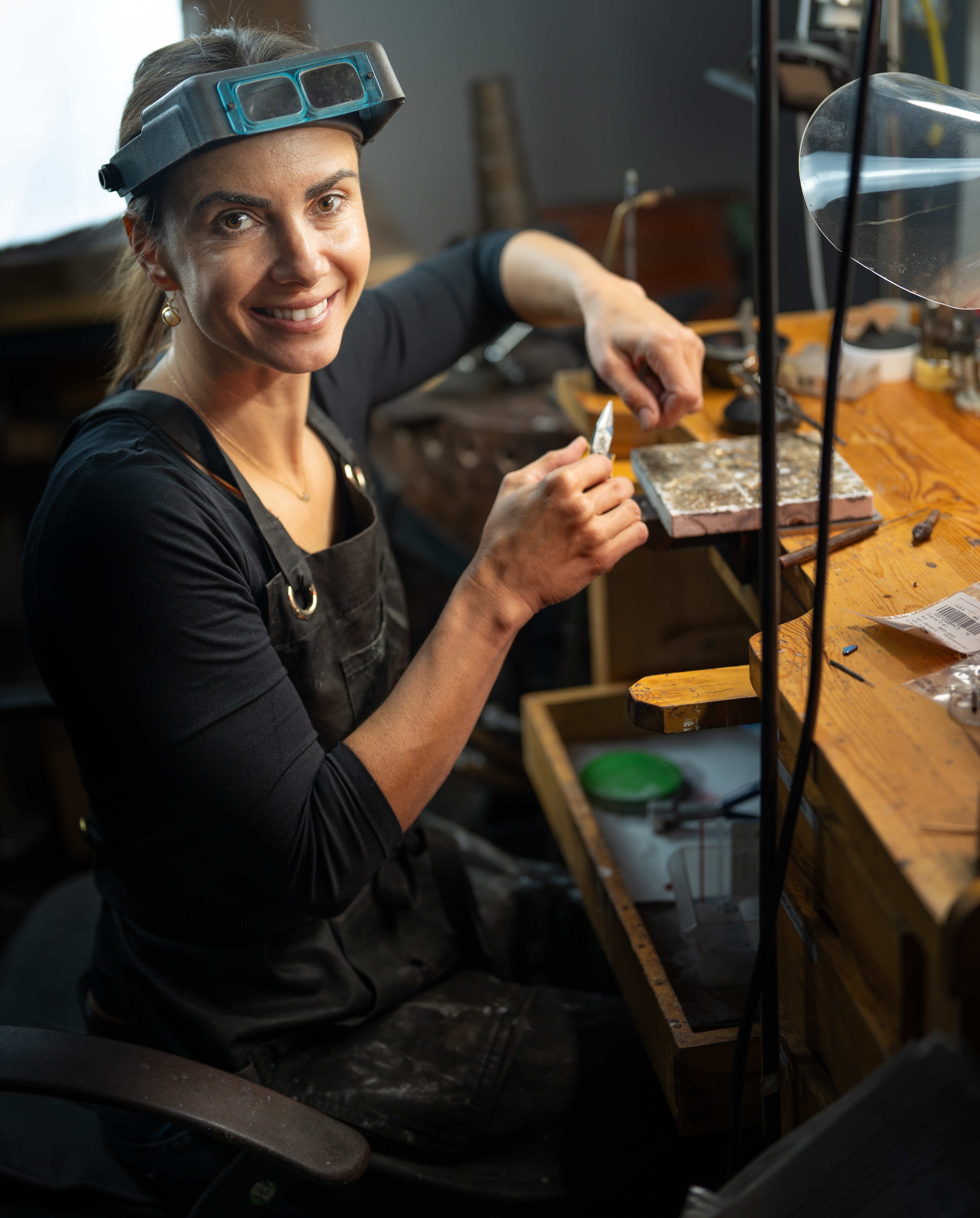 Environmental portrait of a jewelry studio owner smiling at her workbench