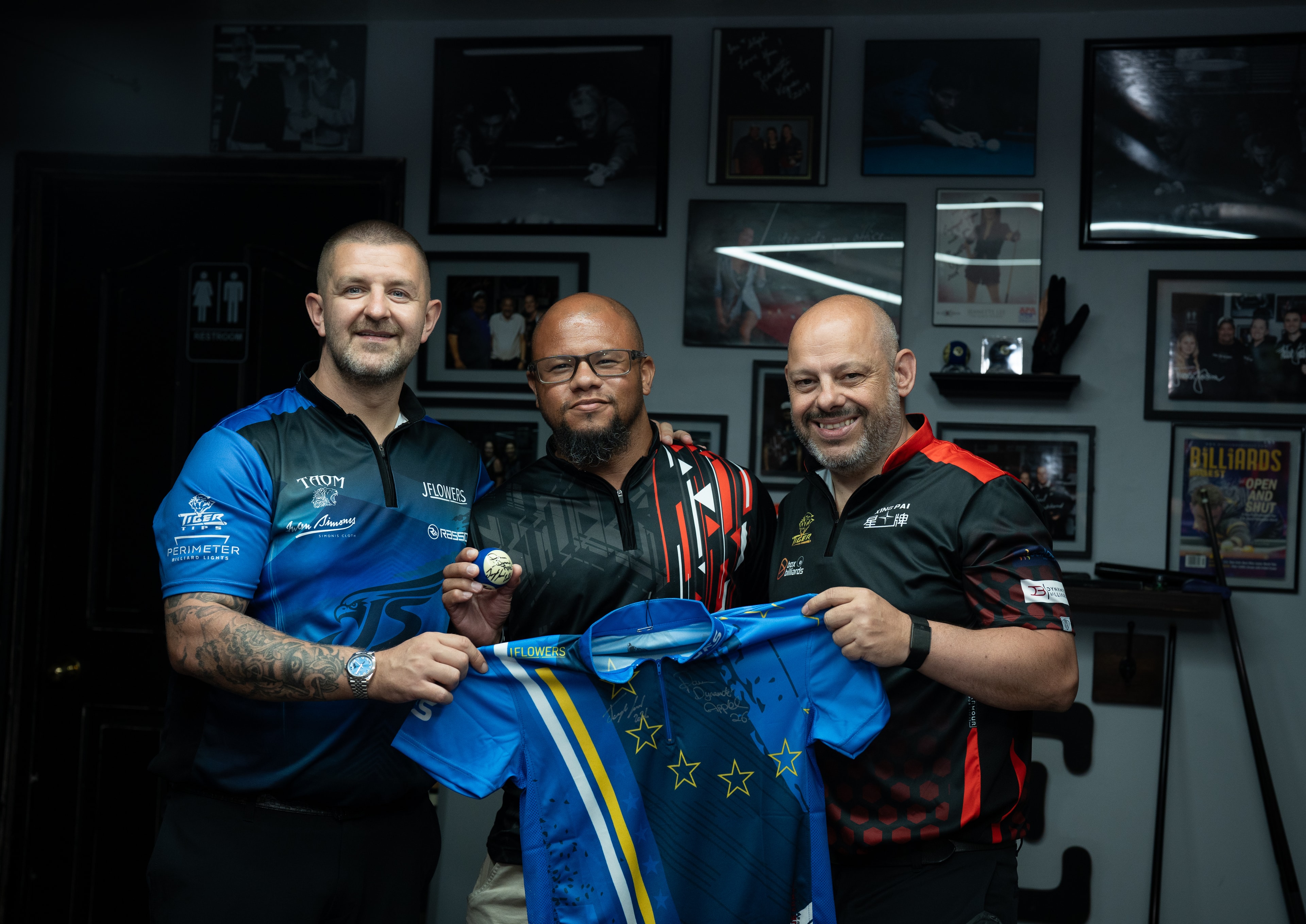 Professional pool players hold a signed jersey in a billiards trophy room