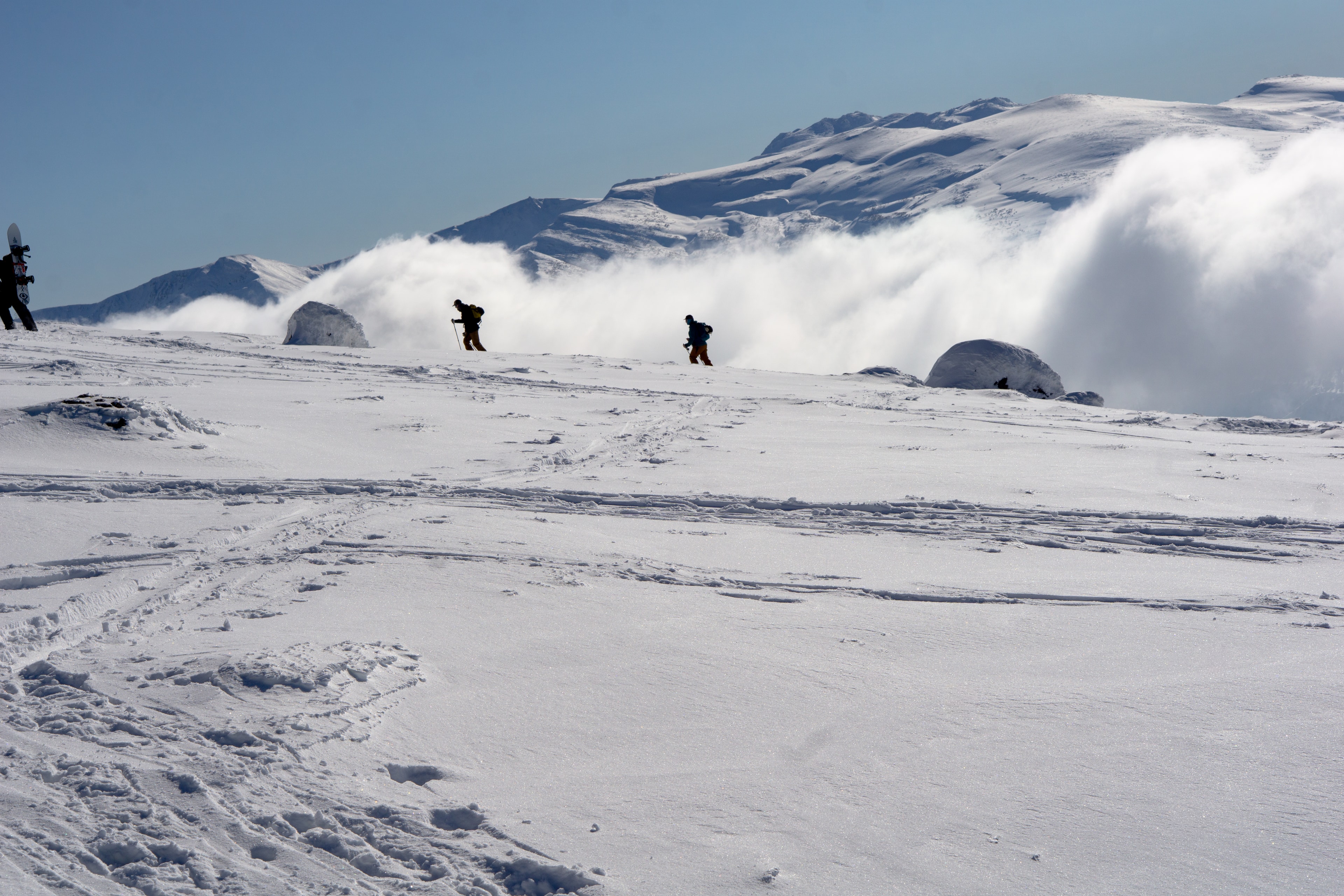 Two ski tourers skinning along a ridge as a cloud inversion breaks over it. Asahi-dake, Japan